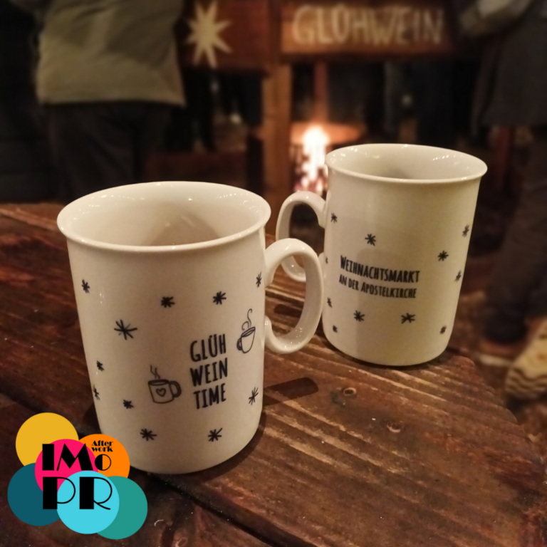 Afterwork Impro auf dem Weihnachtsmarkt an der Apostelkirche: Spielfreude, Glühwein und gute Laune auf dem schönsten Weihnachtsmarkt in Eimsbüttel. Zwischen 18:30 und 20:30 Uhr hast du drei Mal für jeweils 20 Minuten die Möglichkeit, Improtheater auszuprobieren. Im Vordergrund des Bildes sieht man zwei Weihnachtsmarktbecher mit Schriftzügen, im Hintergrund das prasselnde Feuer. Mit Afterwork Impro in den Feierabend starten, entdecke Improvisationstheater an coolen Orten! Afterwork Impro aus Hamburg veranstaltet Business- und Freizeit-Workshops mit den Methoden des Improtheaters.